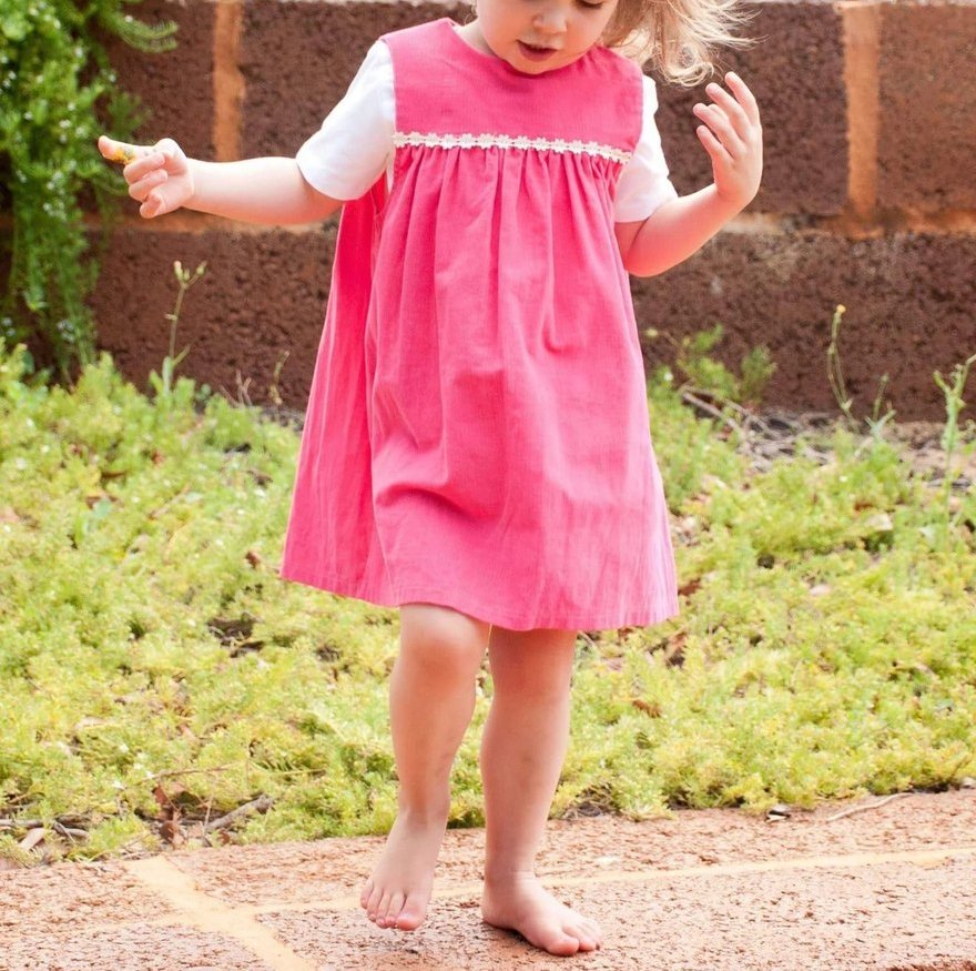 A young child in a pink pinafore playing outdoors
